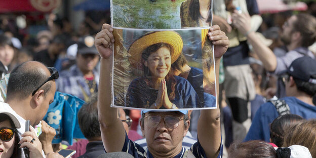 Viele Menschen, einer von ihnen hält ein Plakat der früheren Premierministerin Shinawatra hoch