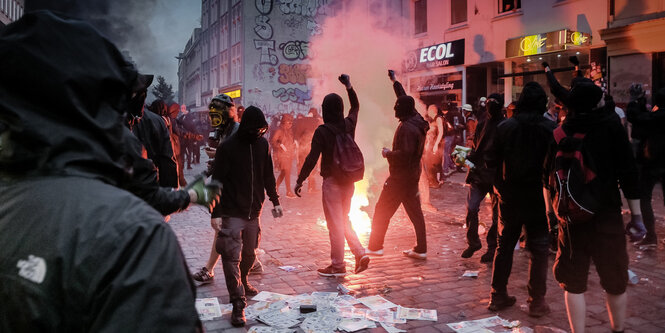 Schwarz vermummte Menschen, erleuchtet von einem Bengalo