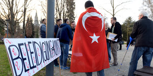 Ein Mensch hat sich die türkische Fahne umgehängt, daneben steht ein Schild mit der Aufschrift „Beleidigung = Kunst“