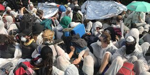 Menschen in weißer Schutzbekleidung sitzen dicht gedrängt am Boden