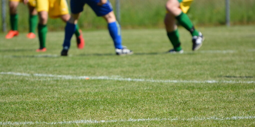 Rasen, im Hintergrund die Beine von Fußballspielern