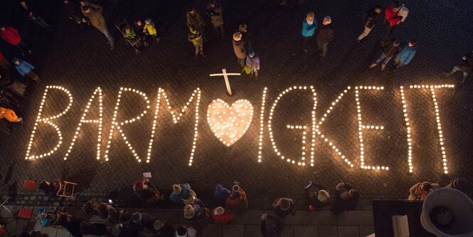 Kerzen formen das Wort Barmherzigkeit. Menschen stehen drum herum