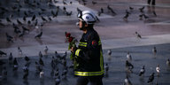 Ein Feuerwehrmann trägt Rosen über einen Platz voller Tauben