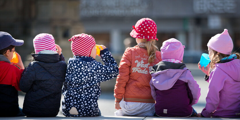 Ein paar Kinder sitzen in Jacken und Mützen gehüllt nebeneinander