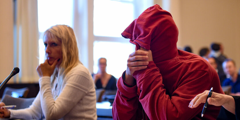 Ein Mann mit rotem Pullover hat die Kapuze übers Gesicht gezogen