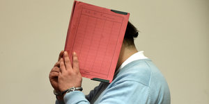 Ein Mann hält sich eine rote Mappe aufgeklappt vors Gesicht