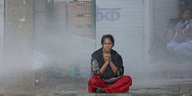 Eine Frau sitzt im Schneidersitz auf einer Straße und wird von einem Wasserwerfer nass