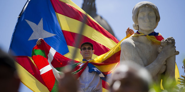 ein Mann mit der Flagge Kataloniens streckt die Arme in die Höhe