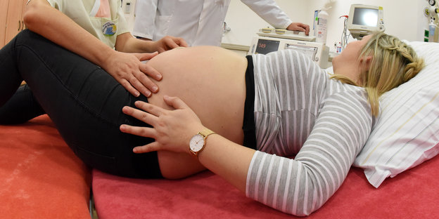 Eine Hebamme tastet einer Schwangeren den Bauch ab.