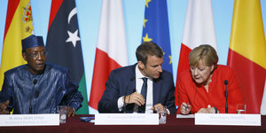 Idriss Deby, Emmanuel Macron und Angel Merkel sitzen nebeneinander an einem Tisch. Macron und Merkel stecken die Köpfe zusammen
