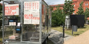 Ein Anhänger aus Glas mit Plakaten vor einem Backsteingebäude