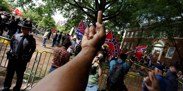 Vor einer Gruppe Menschen, die Konföderiertenflaggen tragen, erhebt sich ein schwarzer Mittelfinger
