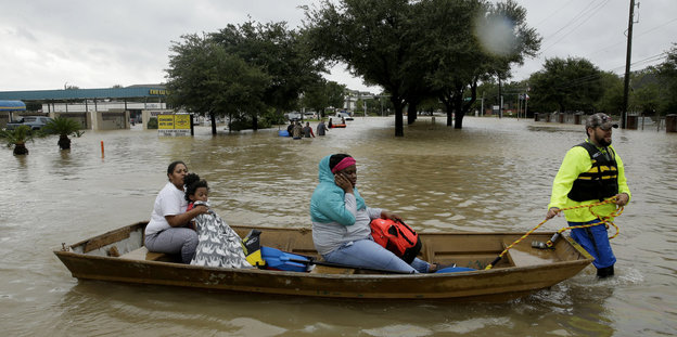 Menschen in einem Boot werden auf einer überfluteten Straße von einem Retter gezogen