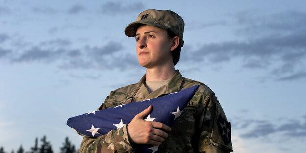 Soldatin vor Abendhimmel mit einer Flagge im Arm