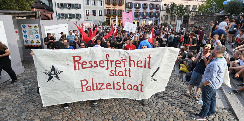 Menschen mit großem Transparent mit der Aufschrift "Pressefreiheit statt Polizeistaat" auf einem Platz in einem Ort