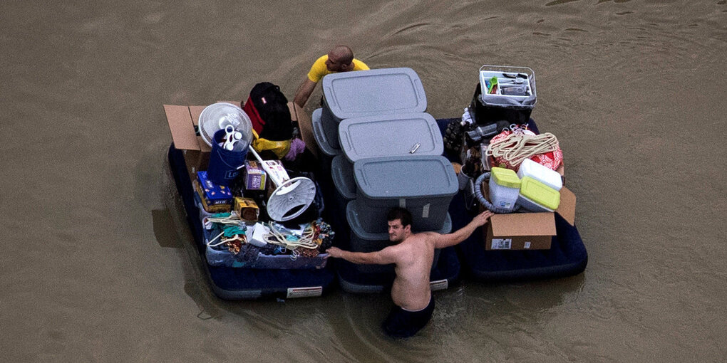 Menschen waten durchs Wasser, schieben drei Luftmatratzen mit Sachen