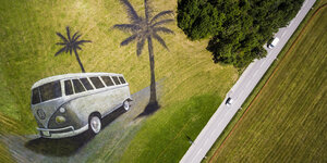 Neben einer Straße ist ein VW-Bus zwischen Palmen auf einen Acker gemalt