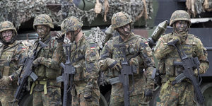 Mehrere Soldaten in Uniform mit geschwärzten Gesichtern und Gewehren