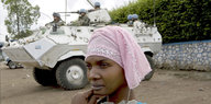 Vor einem weißen UN-Panzer steht eine Frau, die ein rosafarbenes Kopftuch trägt