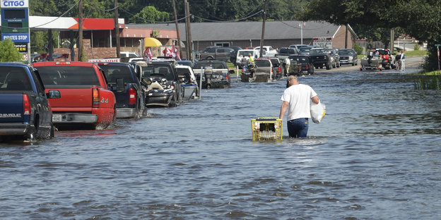 Ein Mann geht auf einer Straße, die fast hüfthoch überschwemmt ist
