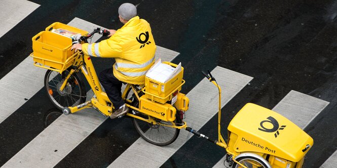 Ein Briefzusteller fährt mit einem Fahrrad über einen Zebrastreifen