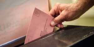 Eine Hand steckt einen Stimmzettel in die Wahlurne