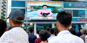 Menschen auf einem Platz sehen auf einem Fernsehbildschirm die Nachrichten