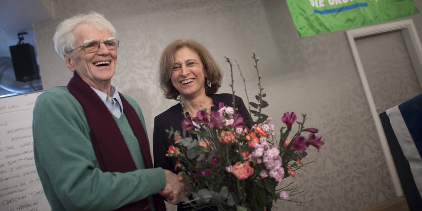 Ein Mann, Ströbele, gibt einer Frau, Bayram, mit Blumenstrauß die Hand