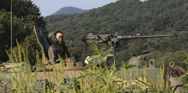Ein Soldat sitzt auf einer Panzerhaubitze, vor ihm Gebüsch, hinter ihm Berge