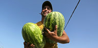 Ein Mann hält zwei große Melonen im Arm