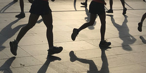 Die Beine joggender Menschen im Abendgegenlicht auf Asphalt