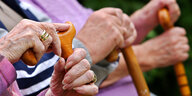 Senioren sitzen in Leichlingen (Nordrhein-Westfalen) auf einer Parkbank und halten ihre Gehstöcke.
