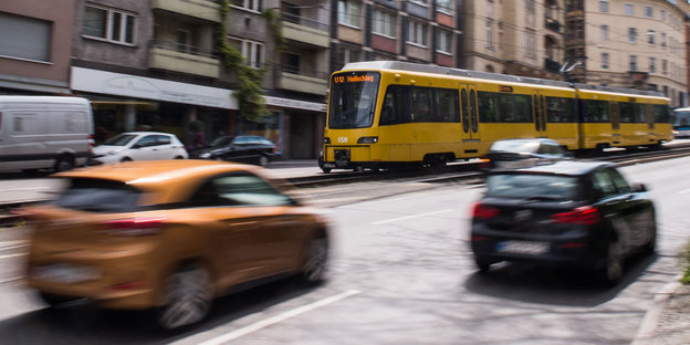 Eine gelbe Straßenbahn fährt in die linke Richtung, zwei durch die Bewegung verschwommene Autos davor in die Gegenrichtung