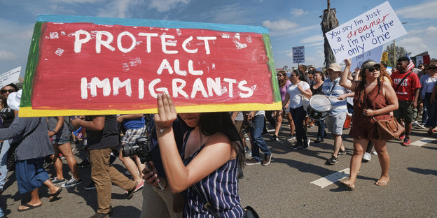 Protestierende, im Vordergrund ein Schild mit der Aufschrift „Protect All Immigrants“