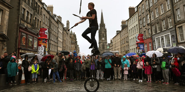 Ein mit Messern jonglierender Mann auf einem Einrad sowie viele Zuschauer