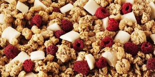 Nahaufnahme von Müsli mit weißen Schokoladenstücken und ganzen Himbeeren