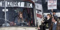 Eine rothaarige Frau lenkt einen Bus mit einem Banner, auf dem "Mein Bauch gehört mir" steht, um sie herum demonstrieren Abtreibungsgegner mit Plakaten