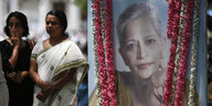 Ein großes und geschmücktes Foto einer Frau, daneben stehen zwei andere Frauen in indischer Kleidung
