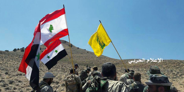 Fahnen der Hisbollah, Libanons und Syriens vor einer kargen Wüstenlandschaft