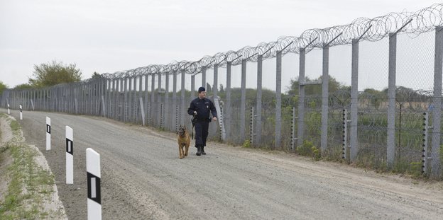 Wachmann mit Hund an einem Grenzzaun