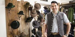 Ein Mann in bayerischer Tracht steht vor einer Hutwand