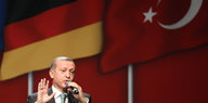 Recep Erdogan steht vor einer deutschen und einer türkischen Flagge und spricht ins Mikrofon