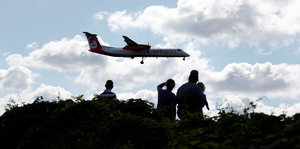 Menschen stehen am Horizont und gucken auf ein landendes Flugzeug