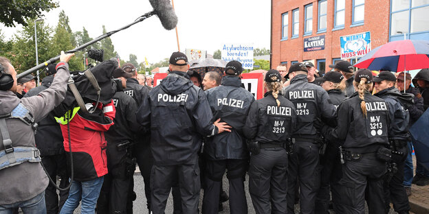 Polizisten von hinten, daneben ein Mensch mit Kamera und einer mit Mikrophon