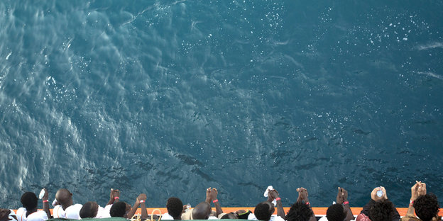 Menschen lehnen sich über die Reling eines Schiffes, unter ihnen: viel türkises Wasser