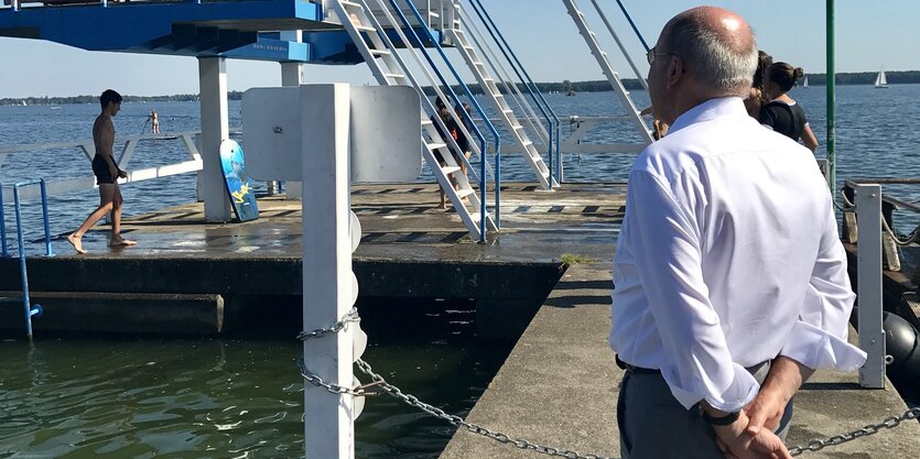 Ein Mann im Hemd schaut auf einen Sprungturm vor einem See