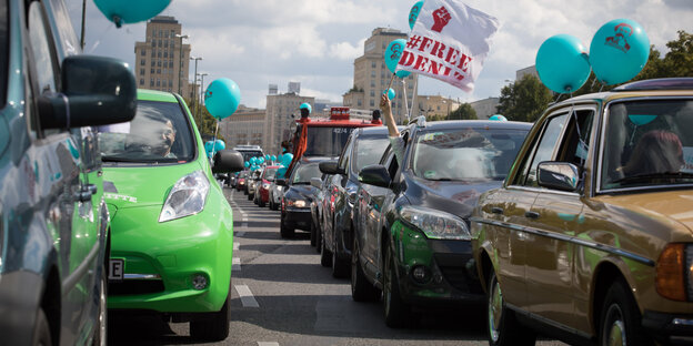 Blaue Luftballons sind an Autos befestigt. Aus einem hält jemand ein Banner mit der Aufschrift „Free Deniz“