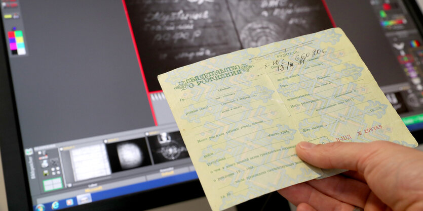 Eine Hand hält ein Blatt Papier vor einem Bildschirm