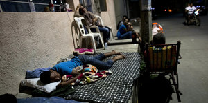 Menschen schlafen in der Nacht auf Matten und Plastikstühlen auf der Straße