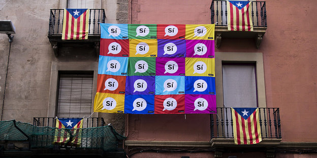 Eine bunte Flagge mit "Sí"-Sprechblasen hängt an einer Hauswand